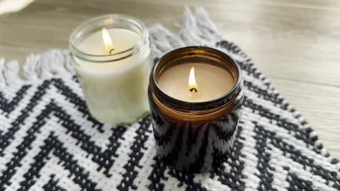 Two burning candles in glass jar on black and white rug on the floor closeup Stock Footage 241246997