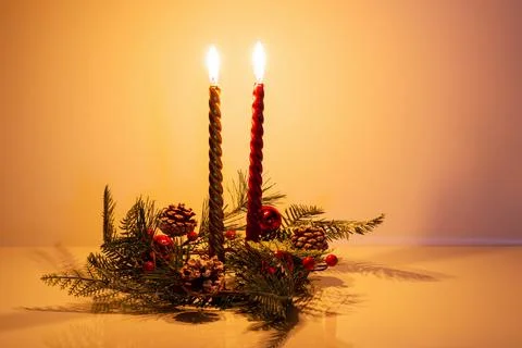 Two burning Christmas candles, gilded and red, in wreath of fir branches Stock Photos