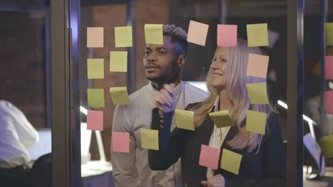 Two business colleagues reading notes on glass wall and discussing strategy Stock Footage 125671561