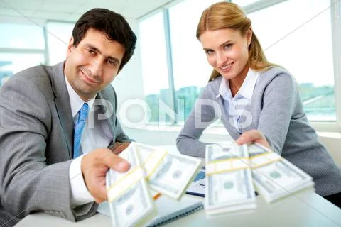 Two business partners at workplace giving money and looking at you Stock-Fotos