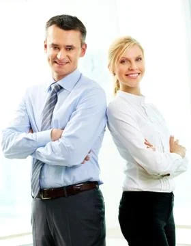 Two business people standing back to back and smiling at camera Stock Photos