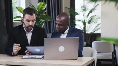 Two business professionals discuss data on a laptop in a modern office Stock Footage 319916240