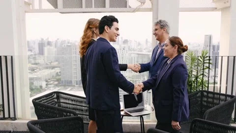 Two business professionals shake hands outdoors on a rooftop, while colleague Video stock 321385672