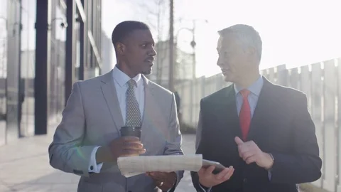 Two business professionals walk and talk over share prices in a paper, in slow m Stock Footage