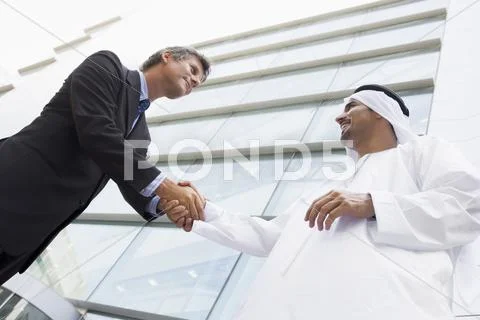 Two businessman outdoors by building shaking hands and smiling (high Stock Photos