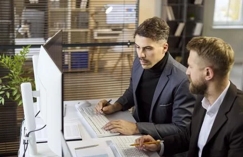 Two businessmen analyzing data on desktop computer at office, finance teamwork Stock Photos