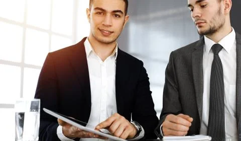 Two businessmen and partners working with tablet computer at the desk in sunny Stock Photos