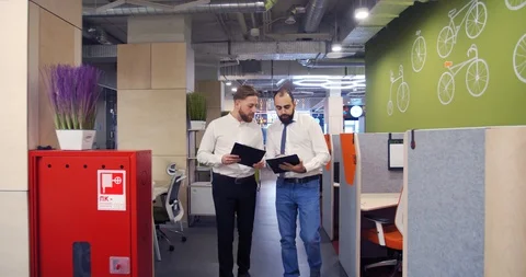 Two businessmen are walking through the office talking to each other, 4k Stock Footage 129322882
