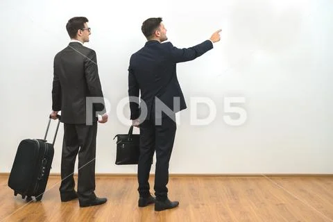 The two businessmen with bags gesture on the white wall background Stock Photos