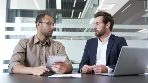 Two businessmen collaborating on a project while sitting at desk at workplace  스톡 동영상 338061272