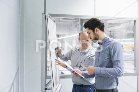 Two Businessmen Having Brainstorm Meeting In Factory Office
