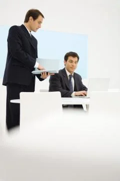 Two businessmen looking at laptop computer together, one holding folder Stock Photos