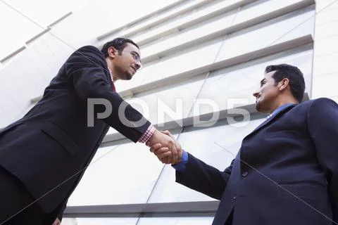 Two businessmen outdoors by building shaking hands (high key/selective focus) Stock Photos