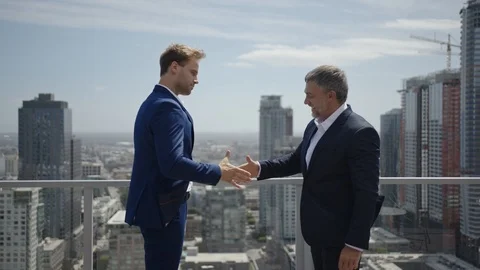 Two businessmen shake hands to complete a deal on rooftop Stock Footage 127413896
