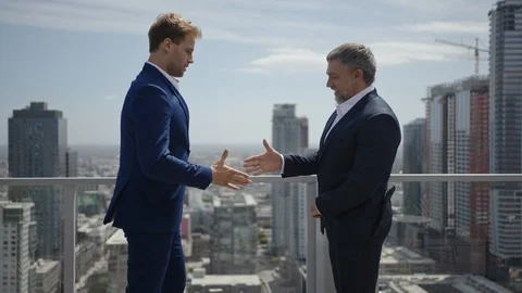 Two businessmen shake hands to complete a deal on rooftop Vídeo Stock 127413917