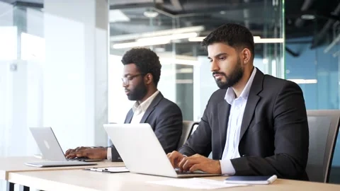 Two businessmen sitting at office desks working on laptop computers Stock Footage 329052401