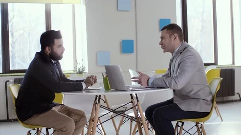 Two businessmen sitting at a round table, are negotiating the upcoming joint Stock Footage 123411515