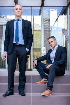 Two businessmen in suits posing outside modern office building, serious look. Foto stock
