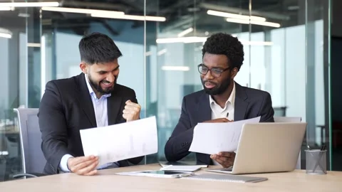 Two businessmen in suits sitting at office desk holding documents and smiling  Stock Footage 329052245