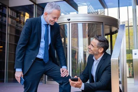 Two businessmen in suits using smartphone outside modern glass office. Foto stock