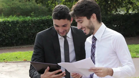 Two businessmen using digital tablet on a park bench Video stock 32580038