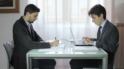 Two businessmen using digital tablet and laptop at desk in office Stock Footage 32626474