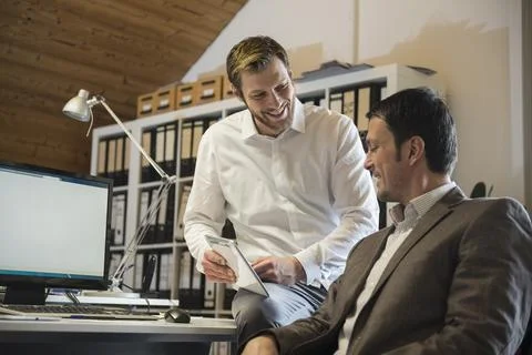 Two businessmen using digital tablet in an office and smiling, Bavaria, Germany Stock Photos