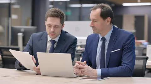 Two Businessmen Working on Laptop with Documents in Office Stock Photos