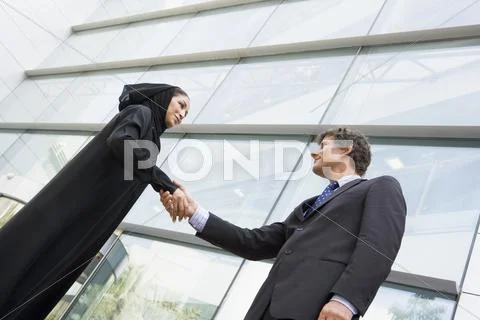 Two businesspeople standing outdoors by building shaking hands and smiling Stock Photos