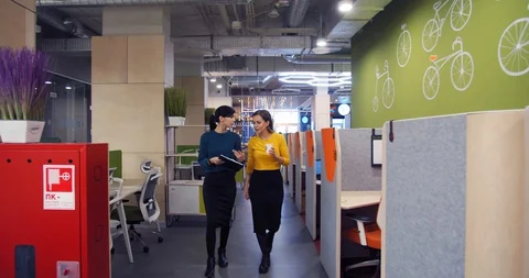 Two businesswomen are talking, walking through the colorful modern office, 4k Stock Footage 129322853