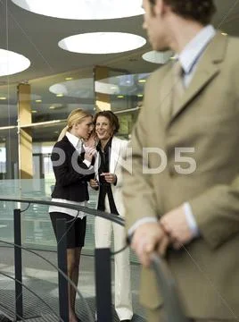 Two businesswomen looking at man, whispering, (focus on background) Stock Photos