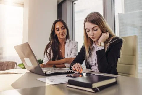 Two businesswomen reading documents using tablet computer sitting at desk in Stock Photos