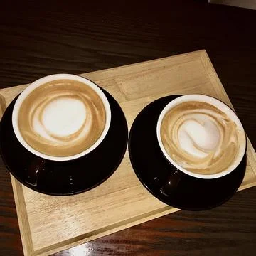 Two café latte cups on tray with creamy foam and premium coffee beans! city moca Stock Photos
