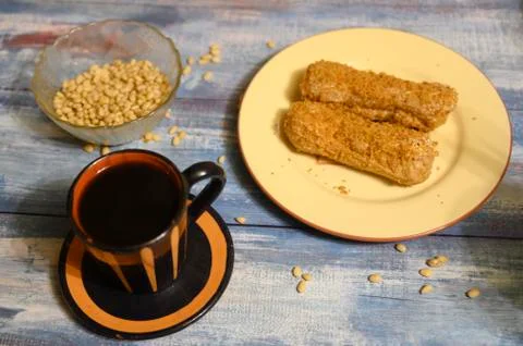 Two cakes on a plate, pine nuts and a mug of coffee on a wooden background. Stock Photos