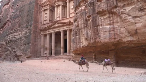 Two camels ride past the Treasury in the ancient city of Petra in Jordan Stock Footage