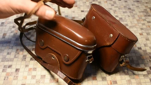 Two cameras in brown leather cases, one of the bottom is taken by a person, then Stock Footage 122625578