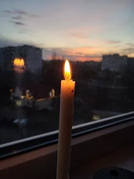 Two candles burning by window at sunset Stock Photos