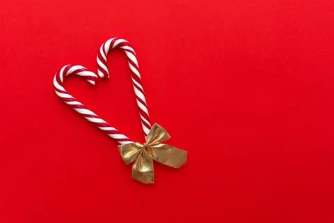 Two candy canes with bow making a heart on a red background. Stock Photos