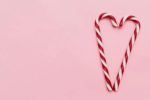 Two candy canes forming a heart shape, on pink background with copy space. .. 스톡 사진