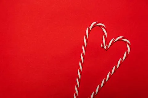 Two candy canes making a heart on a red textured background. Minimalistic chr Stock Photos