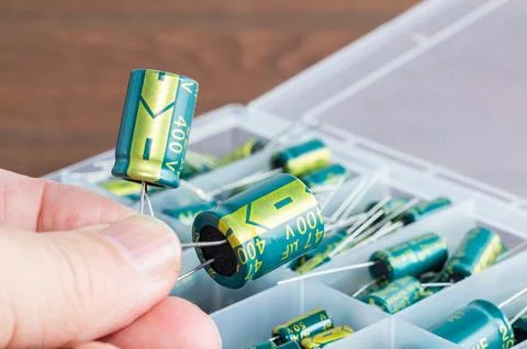Two capacitors held in a hand, with a box of capacitors in the background. Foto stock