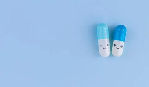 Two capsules with funny faces on blue background top view Stock Photos