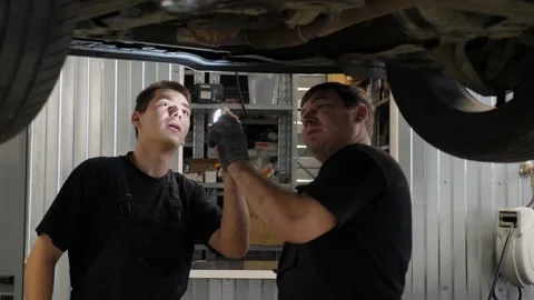 Two car mechanics working under the car on a lift in the garage. Car repair shop Stock Footage 297845148