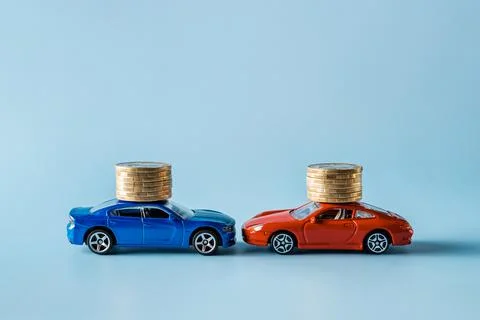 Two car models with coin stacks are head to head against blue background. Stock Photos