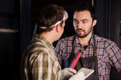 Two carpenters are talking while holding papers and ruler. One of them is Stock Photos