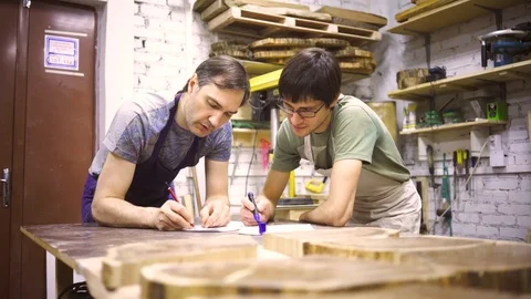 Two carpenters discuss drawing (round wood) in the workshop Stock Footage 102567210
