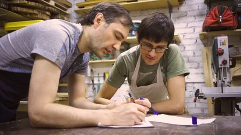 Two carpenters discuss drawing (round wood) in the workshop Stock Footage 102567314