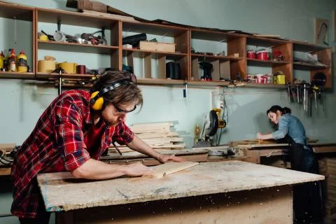 Two carpenters work hard in the workshop. A man and a woman. Stock Photos