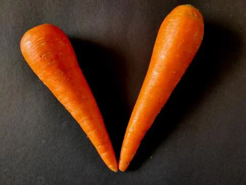 Two carrots kept like V shape. Isolated on black background. Stock Photos