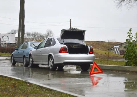 Two cars and a red triangular sign at the scene of an accident on a wet road Stock Photos